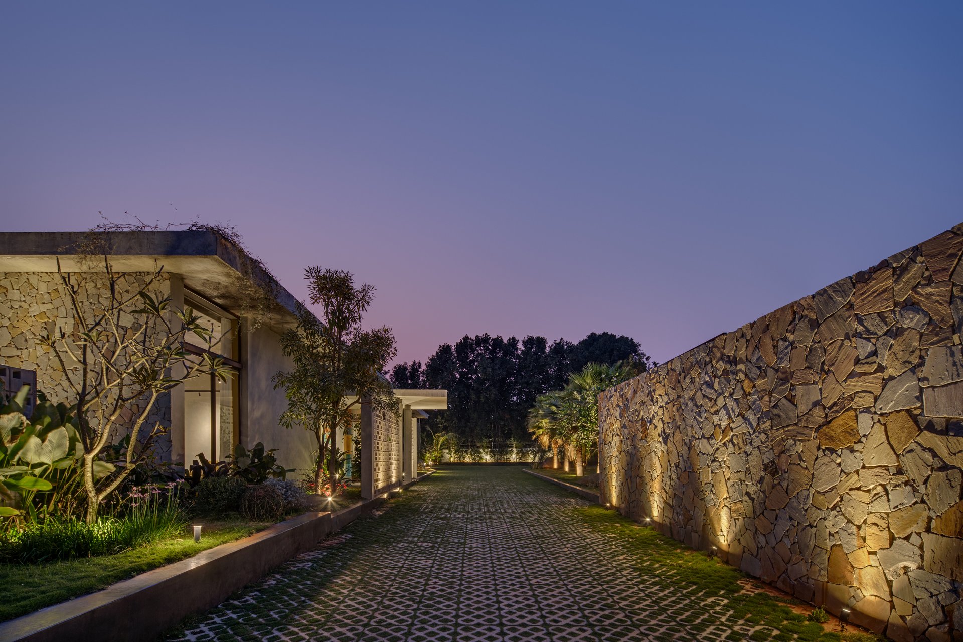 Evening driveway with stone wall illuminated by uplights